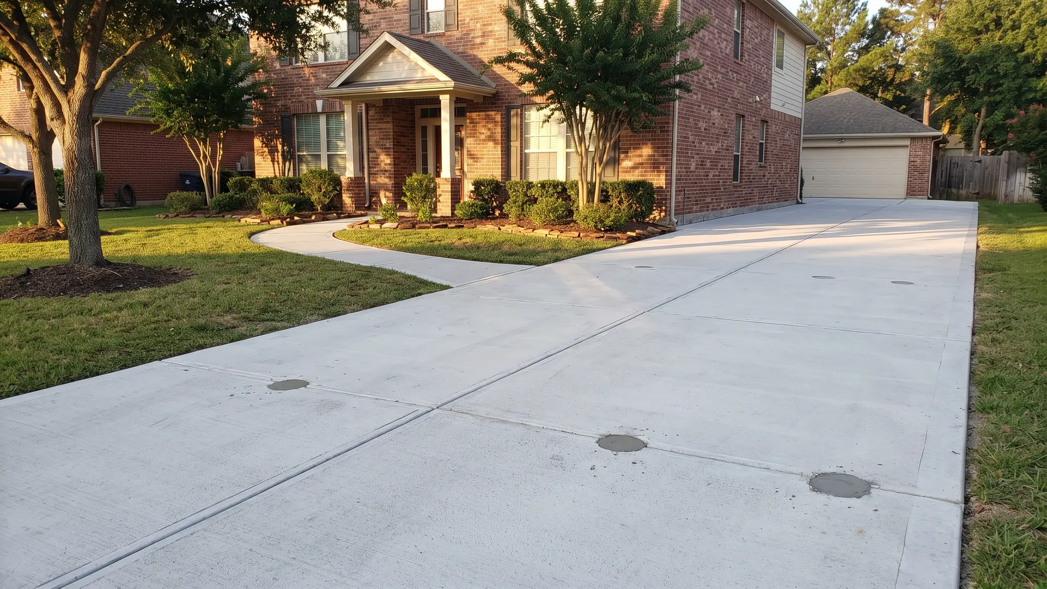 Concrete leveling | Music City Foundation A long freshly leveled concrete driveway and walkway in front of a brick home with a few small round injection holes patched in morning light