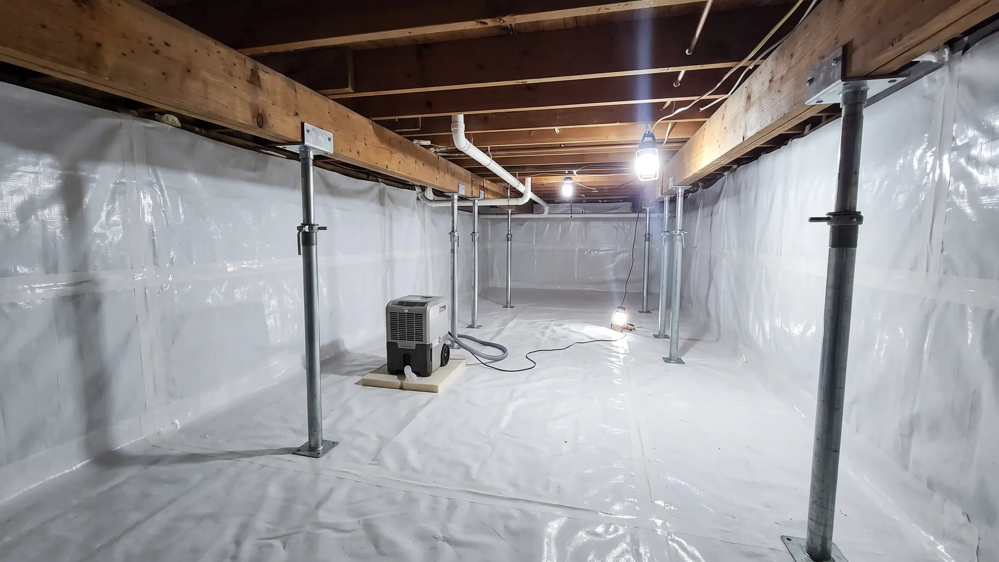 Crawl spaces | Music City Foundation A fully encapsulated crawl space with a bright white vapor barrier on the floor and walls, steel support jacks under the beams and a small dehumidifier