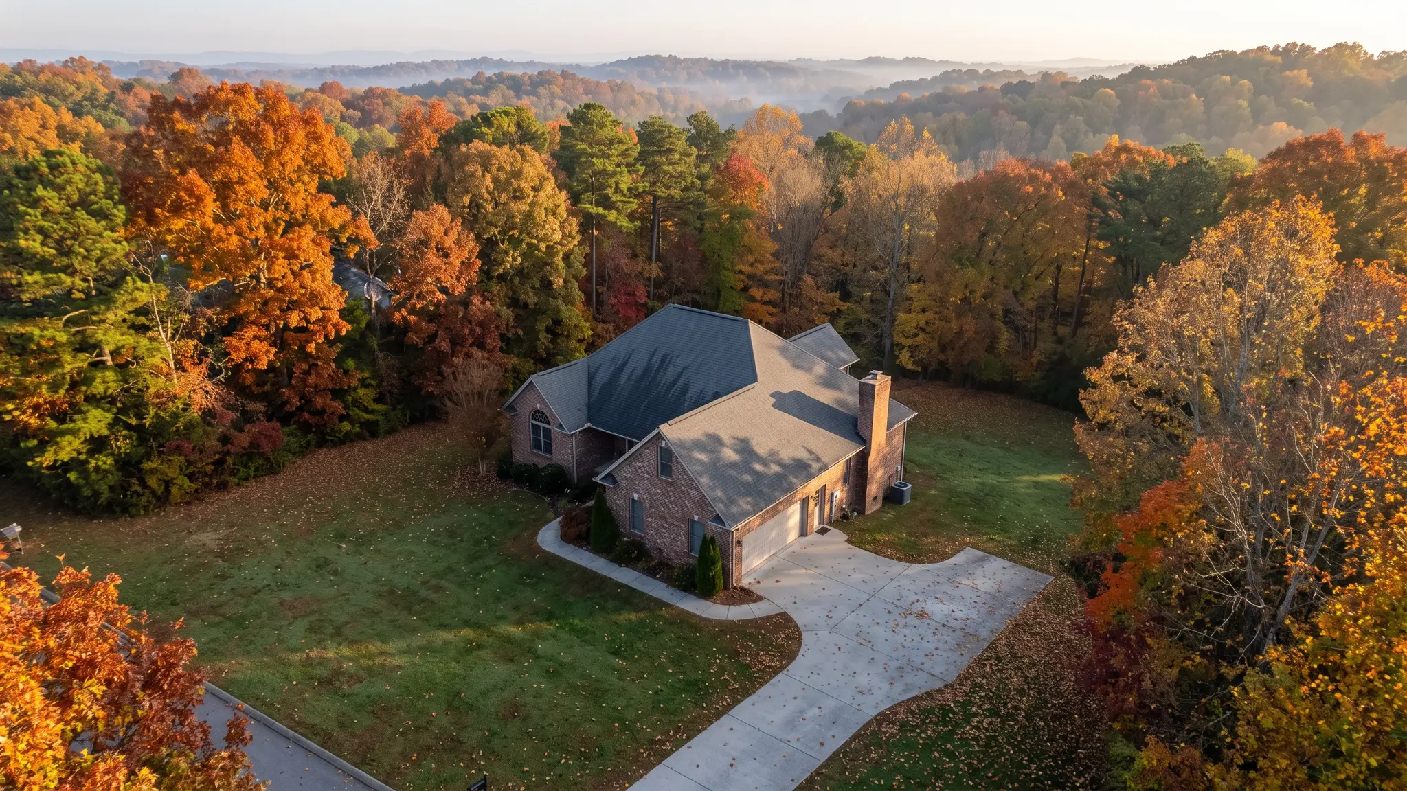 Our foundation process | Music City Foundation An aerial view of a Tennessee residential rooftop and brick home with a green lawn and a driveway among autumn trees in soft morning light